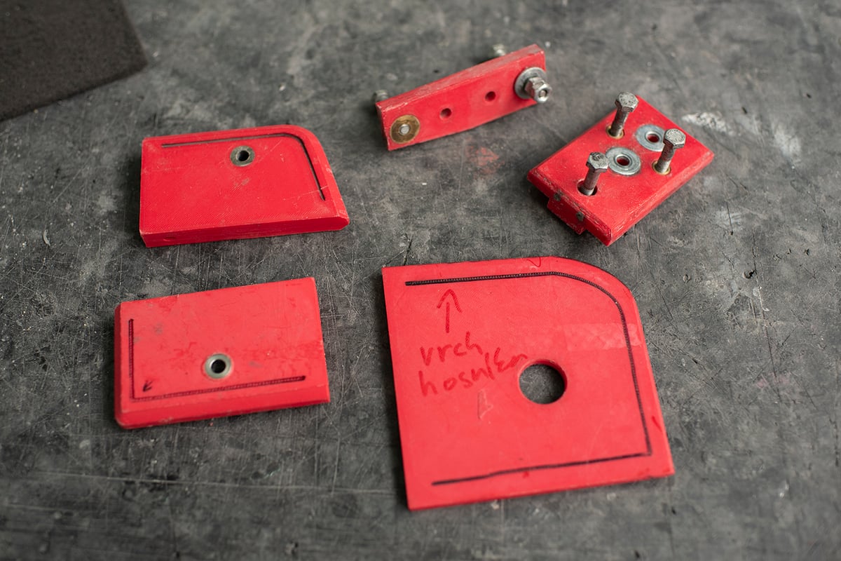 Red 3D printed jigs and drilling templates laid out on a workshop bench