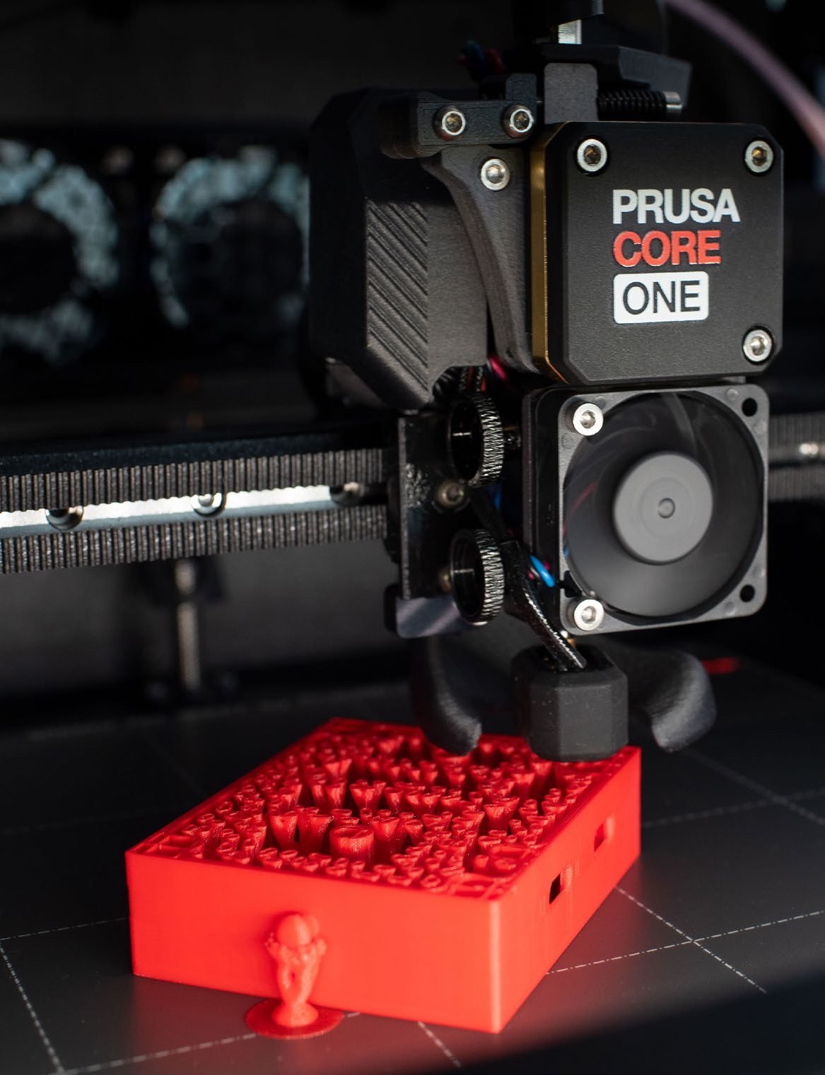 A Prusa CORE One printing a red electronics case