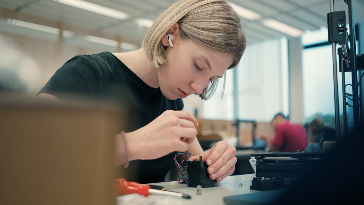 A student screwing together a stepper motor at a studio table, with printer frame parts beside her
