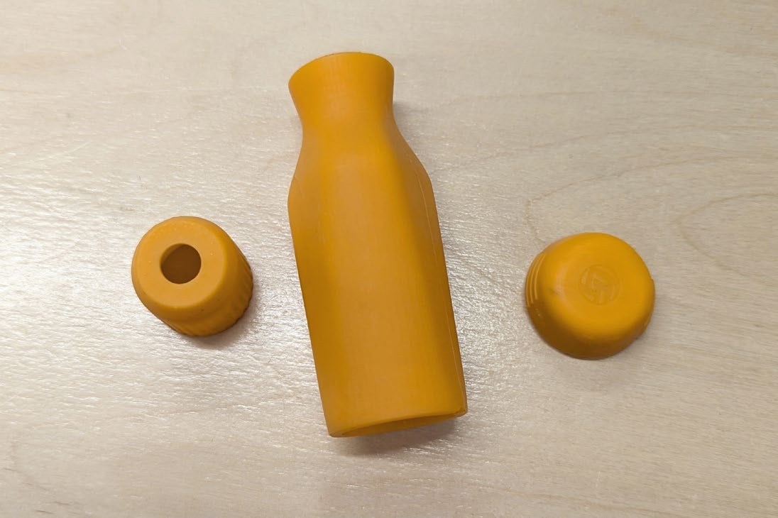 Three amber resin parts on a plywood bench: a collar, a handle body and an end cap embossed with the LTT logo