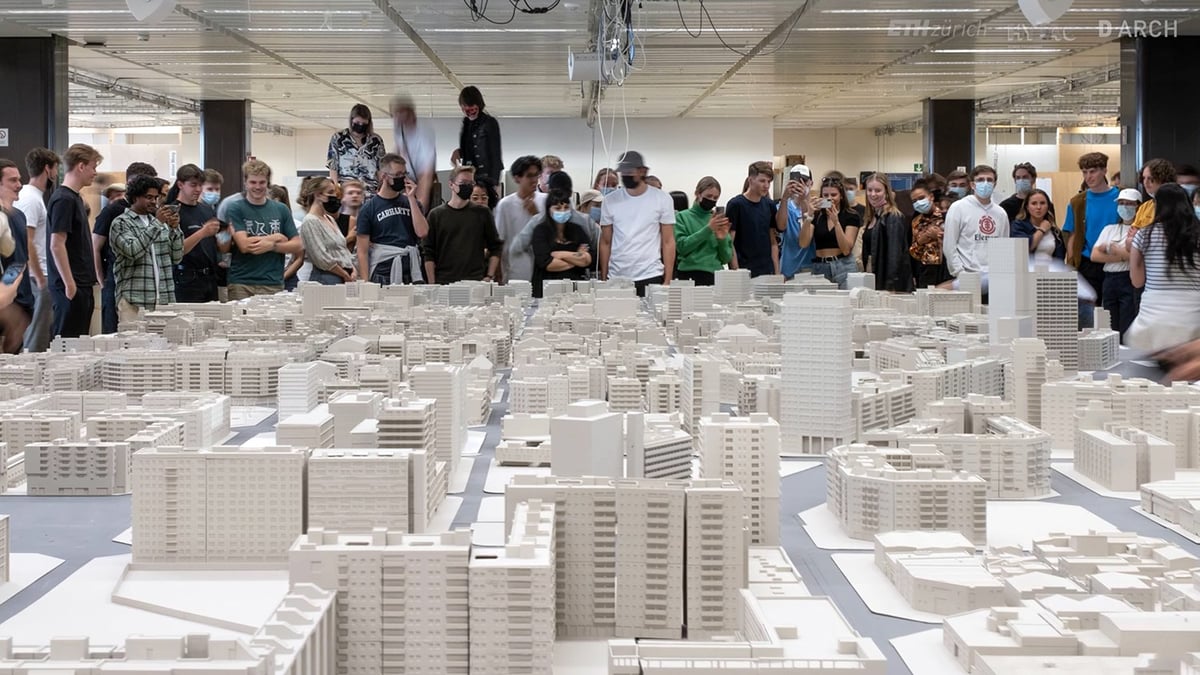 A very large white printed city model filling a room, with a crowd of students standing around it