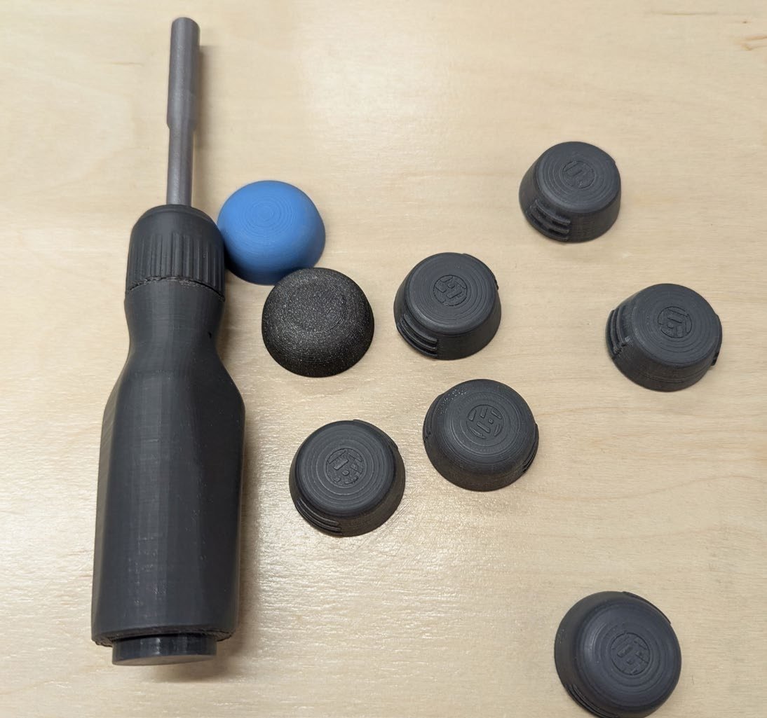 A matte black printed screwdriver body with the steel shaft fitted, surrounded by eight printed end cap prototypes