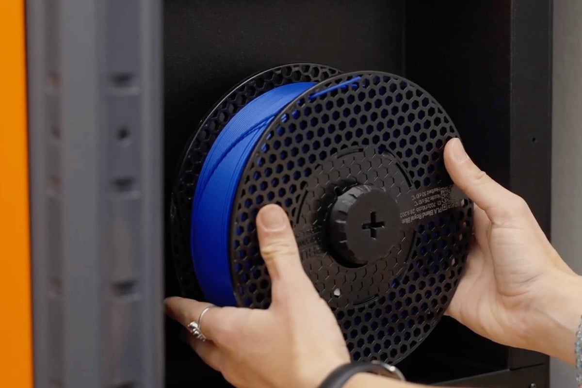 Hands setting a blue Prusament spool onto the holder inside a CORE One