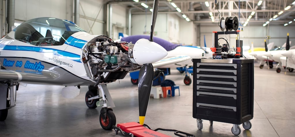 Prusa printer running on a tool cart beside an ultralight aircraft in the Shark.Aero hangar