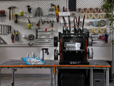 An Original Prusa XL with five toolheads on a bench, printed parts and filament spools around it