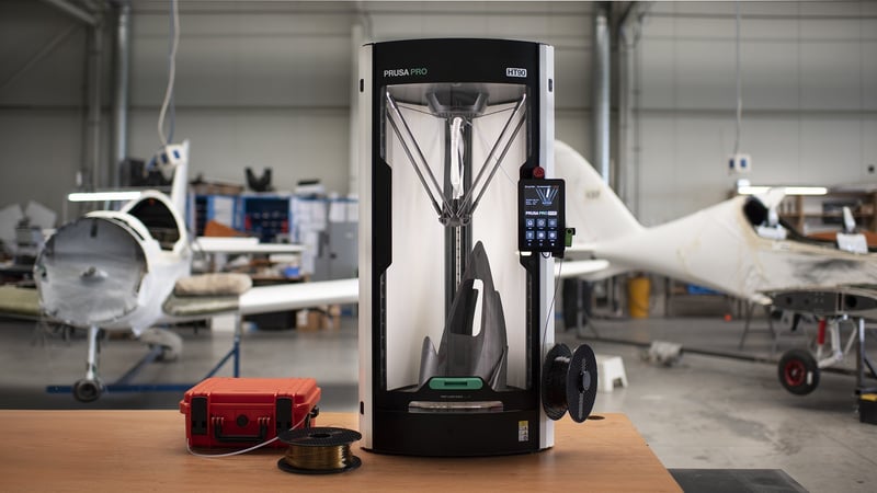 A Prusa Pro HT90 standing in an aircraft hangar beside a light plane