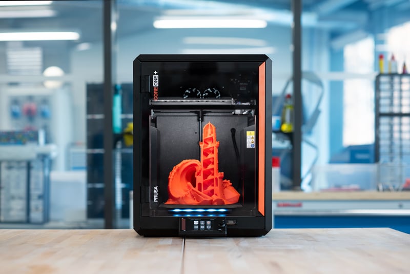 The Prusa CORE One+, a fully enclosed CoreXY printer with an orange cross printed inside